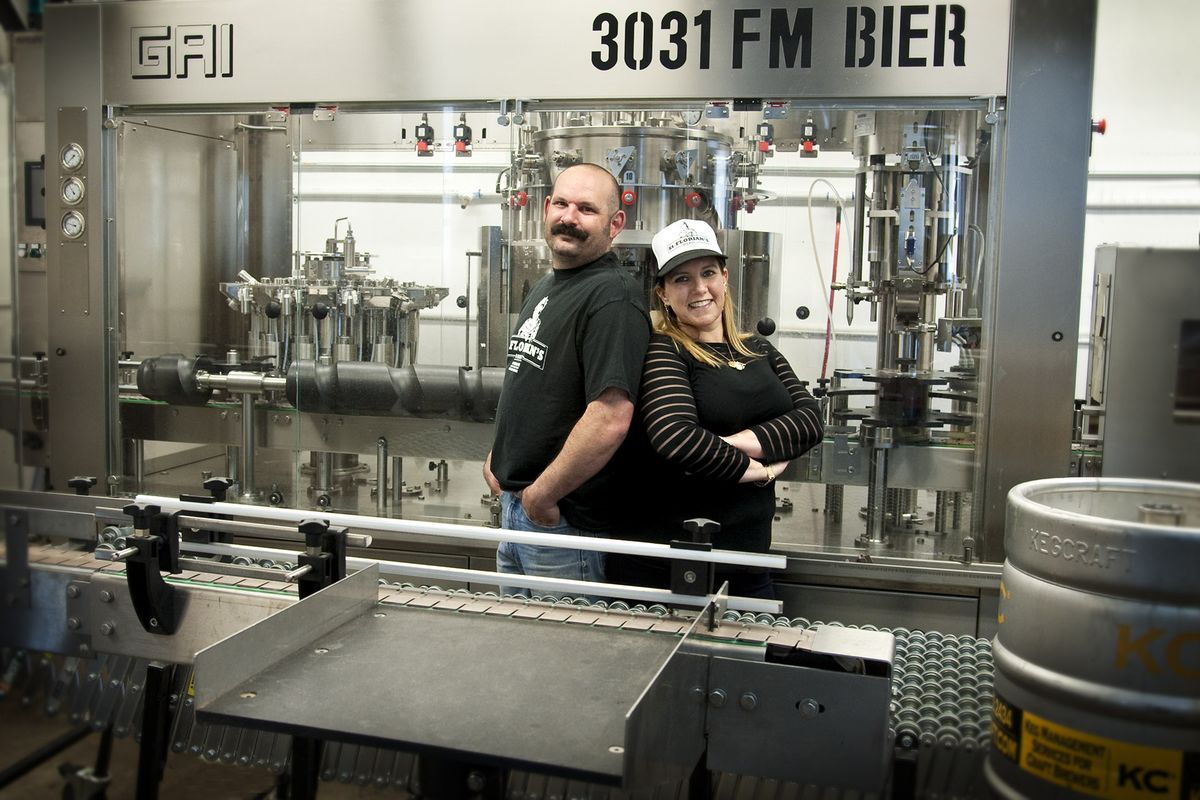Man en vrouw omringd door apparatuur voor het bottelen van bier