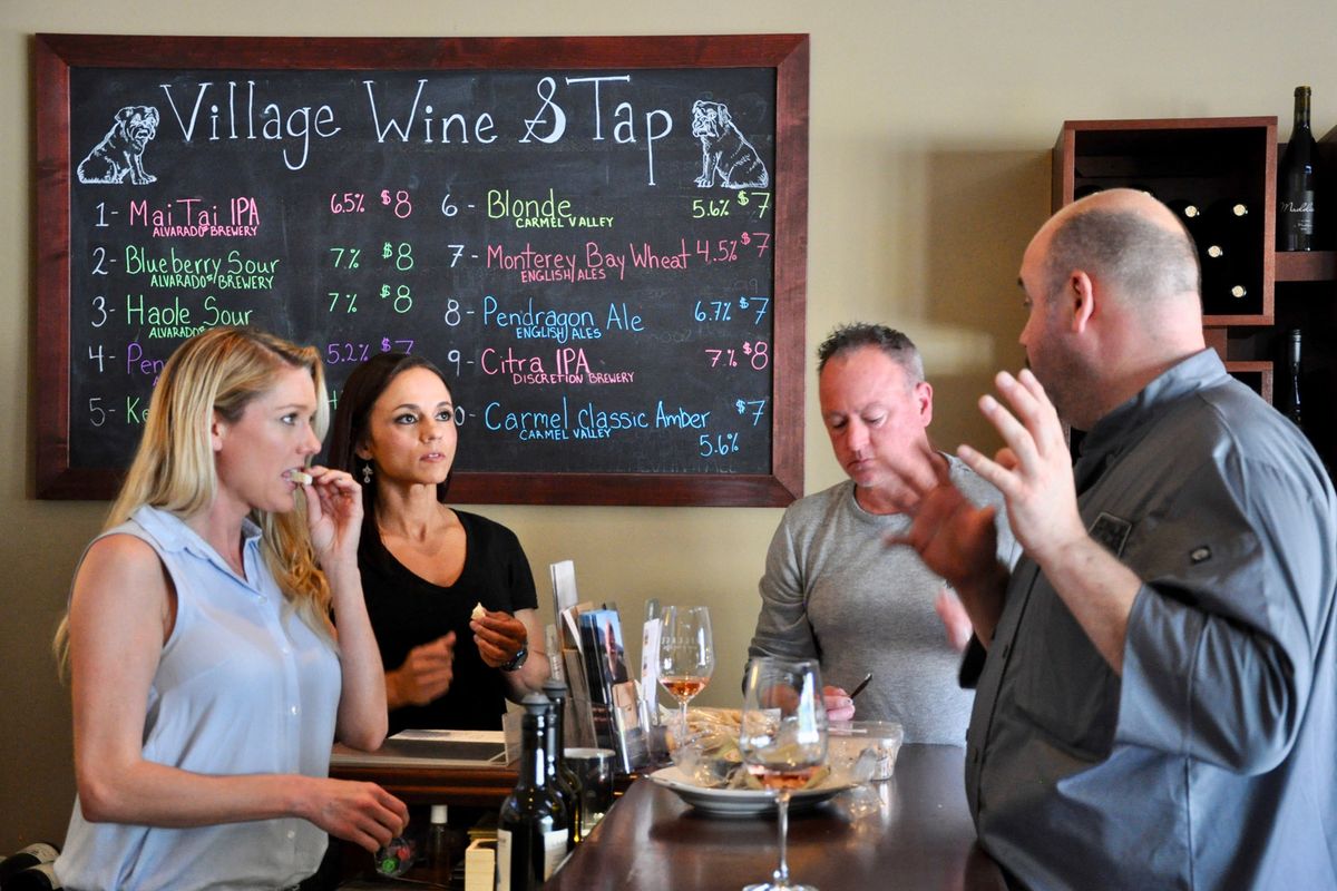 ビールの蛇口リストを示す黒板看板の前にある木製のハイトップテーブルにいる2人の女性と2人の男性