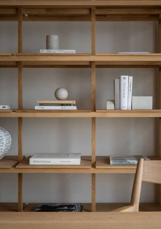 minimalisticky zdobená drevená polica s umeleckými predmetmi, knihami a drevenou stoličkou