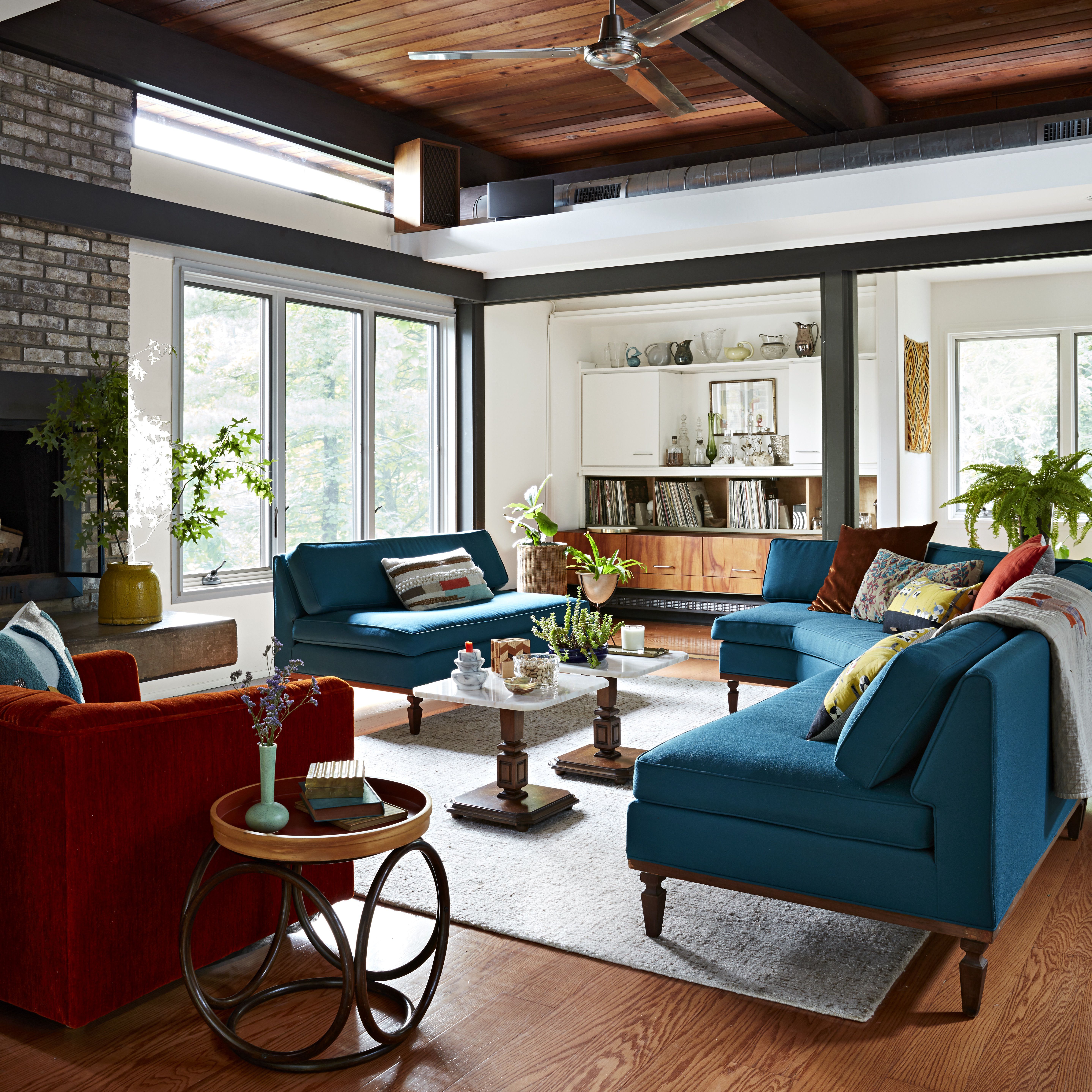 BHG Adoff House Story: современная гостиная середины века с каменным камином, ярко-оранжевыми и бирюзовыми диванами и стульями.