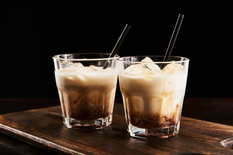   Cocktail russe blanc rumchata dans des verres avec des pailles sur planche de bois isolé sur noir