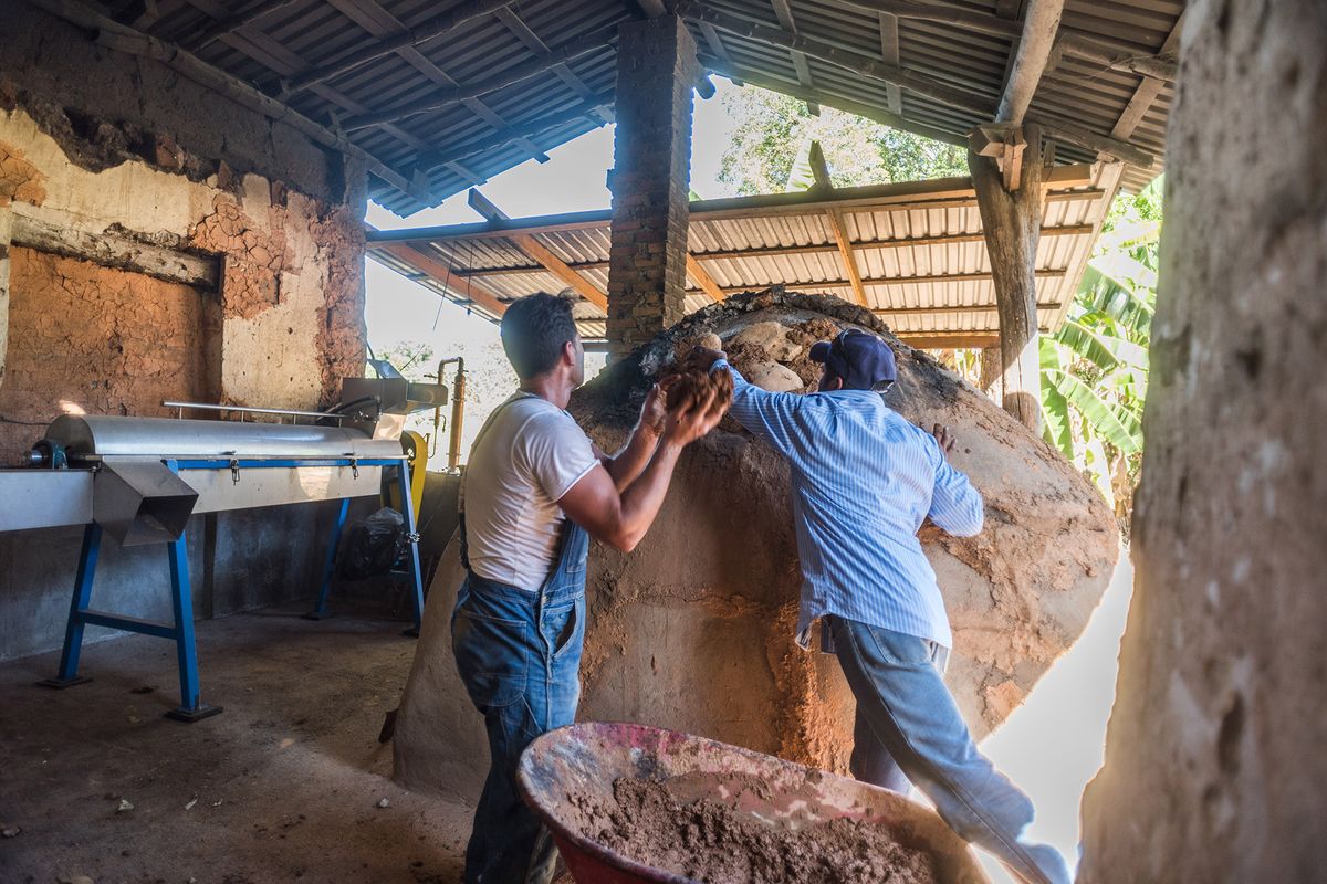 Dos hombres sellando un horno de barro con barro y piedras