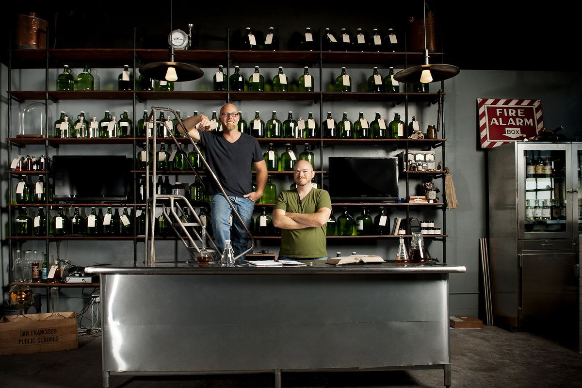 Due uomini in piedi davanti a un muro di bottiglie di vetro