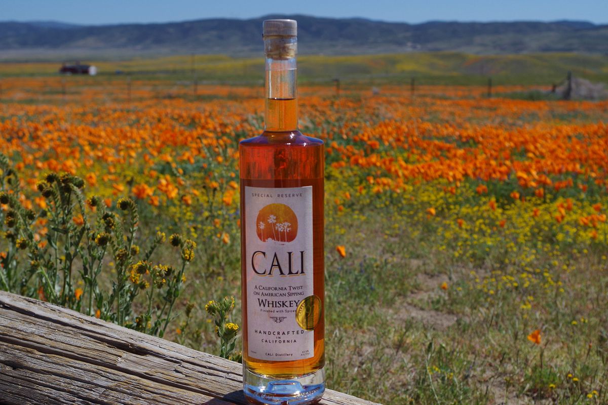 Tanka steklenica viskija pred poljem cvetočih makov