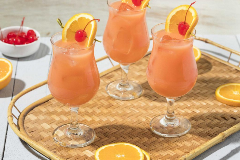   Trei cocktail-uri Hurricane pe tavă cu garnitură de portocale și cireșe