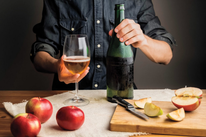   Mãos masculinas segurando uma garrafa de cidra de maçã dura premium na mesa de madeira rústica.