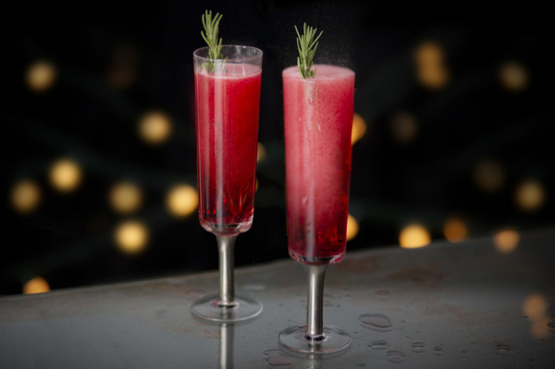   Dva šumivé tmavě růžové nápoje ve flétnové sklenici s rozmarýnovým zdobením
