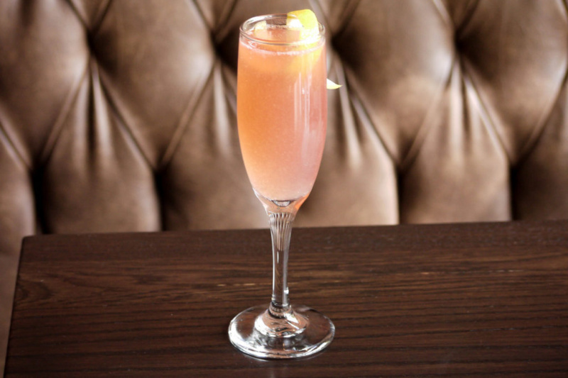   Růžový perlivý nápoj s citronovým zákrutem ve flétně na dřevěném stole