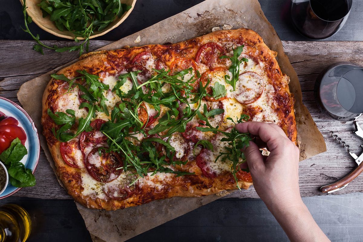 Préparer une pizza gastronomique avec des tomates anciennes et de la roquette. Gros plan, de, garniture main, pizza, à, roquette, vue dessus