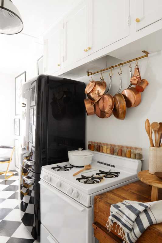 Küche mit weißem Herd, schwarzem Kühlschrank und hängendem Kupfergeschirr