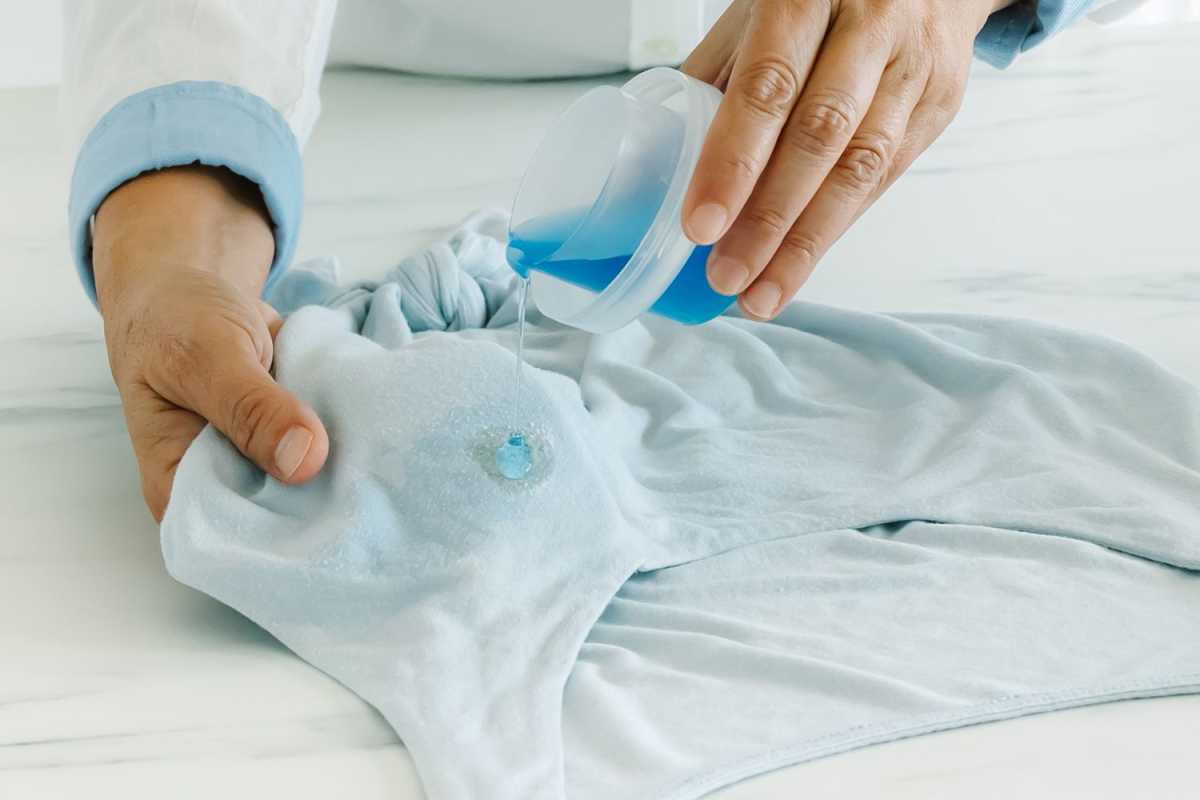 persona que utilitza detergent líquid per eliminar les taques de greix de la roba