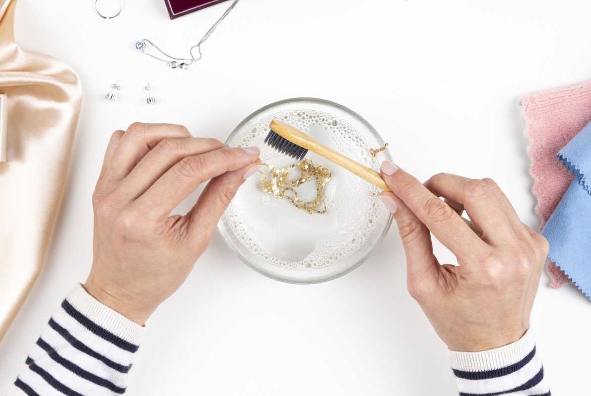 χέρια που χρησιμοποιούν οδοντόβουρτσα για να καθαρίσετε το χρυσό κολιέ