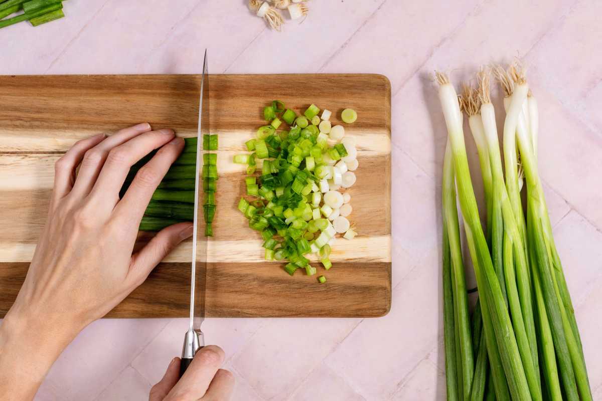 Cortar cebollas verdes en una tabla de cortar.
