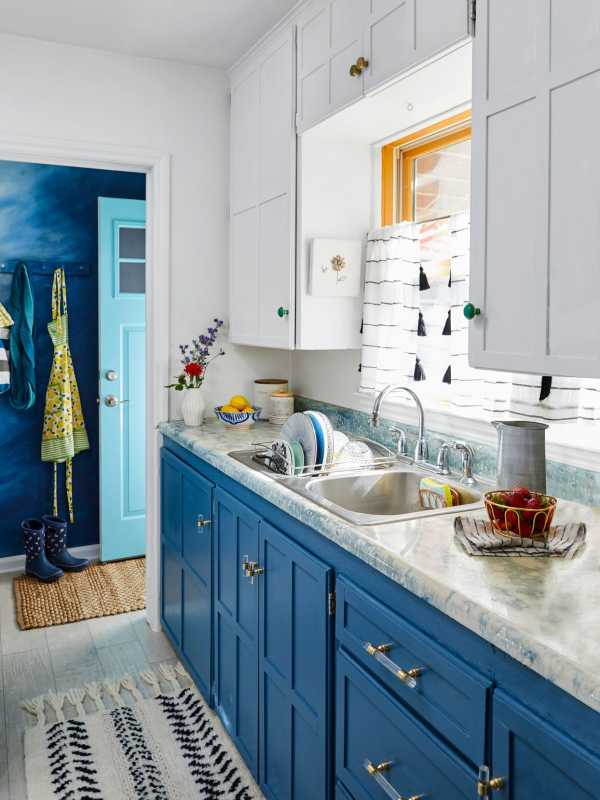køkken med hvide skabe ovenpå og blå forneden og lyse gardiner