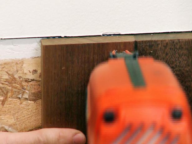Memasang panel kayu wainscoting ke dinding menggunakan pistol paku.