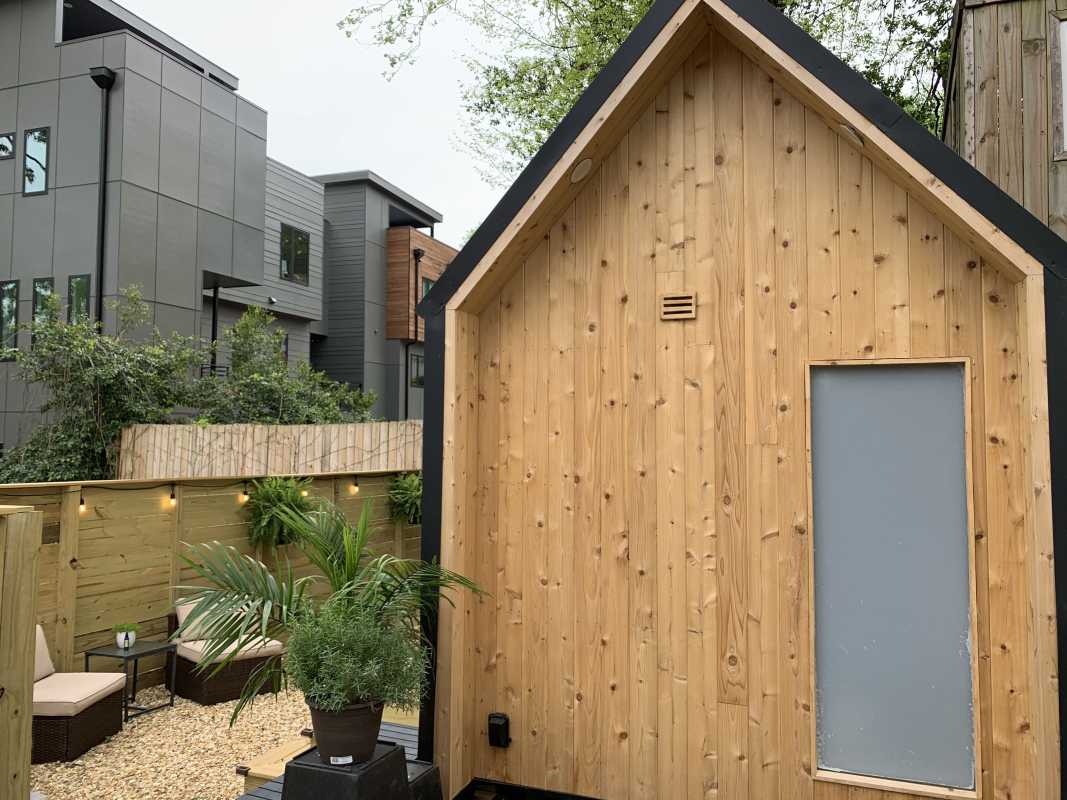 Uma pequena casa de madeira com área de estar ao ar livre cercada.