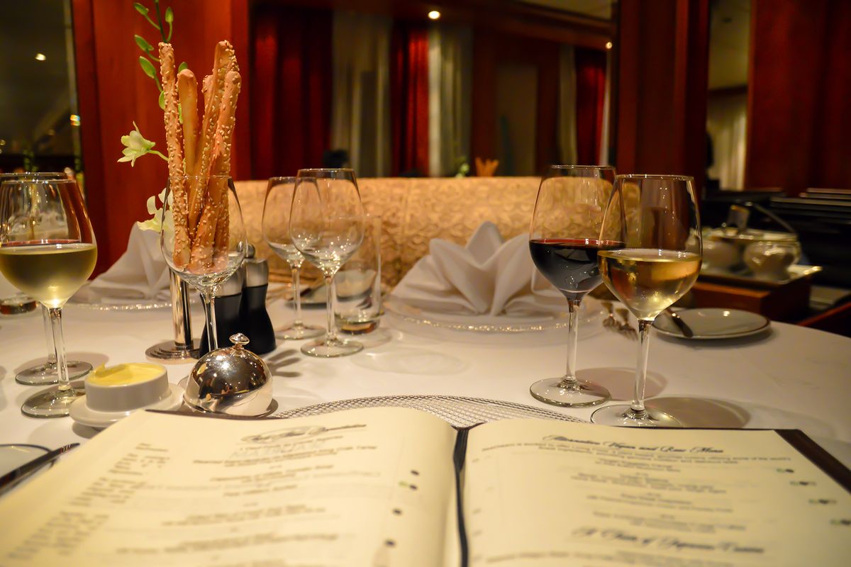 Отворено меню, чаши вино и галета в официална обстановка на маса