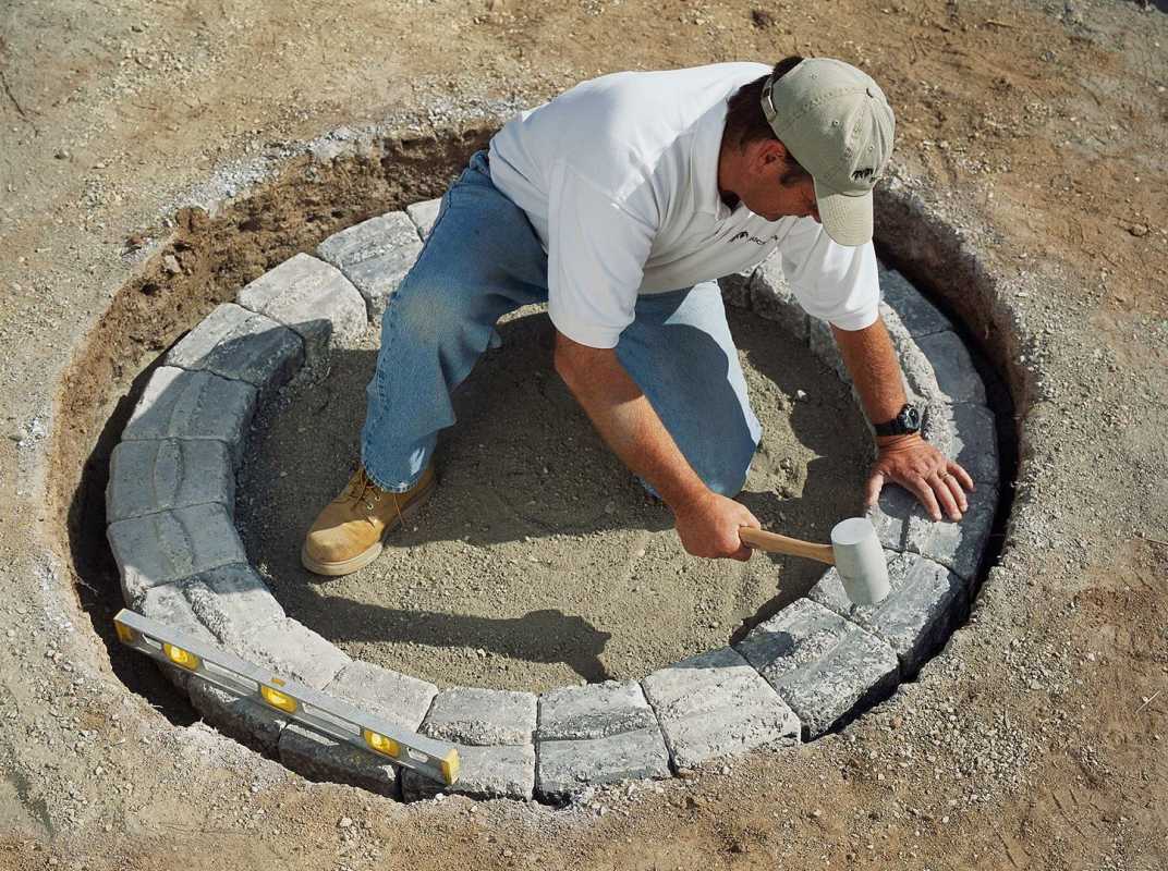 мъж, използващ чук, за да опакова каменна тухла в яма