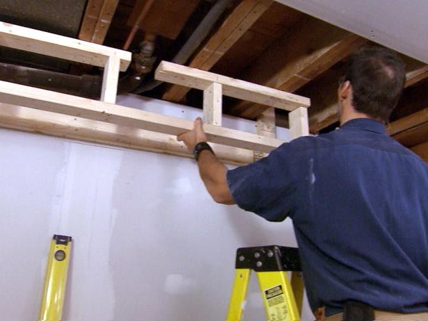 المقاول على سلم أثناء تثبيت إطار صندوق خشبي في مشروع إصلاح المنزل هذا.