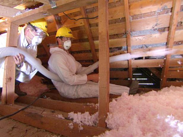 制服を着た2人の男性が、屋根裏部屋の断熱材を空間に吹き付けます。