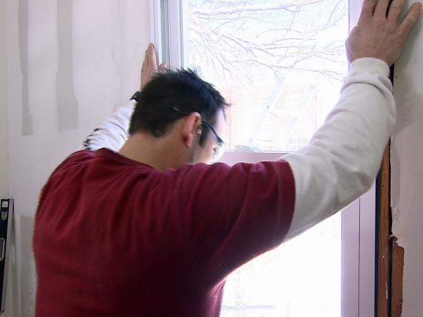 Човек инсталира нов прозорец в тази рамка на този проект за подобряване на дома.