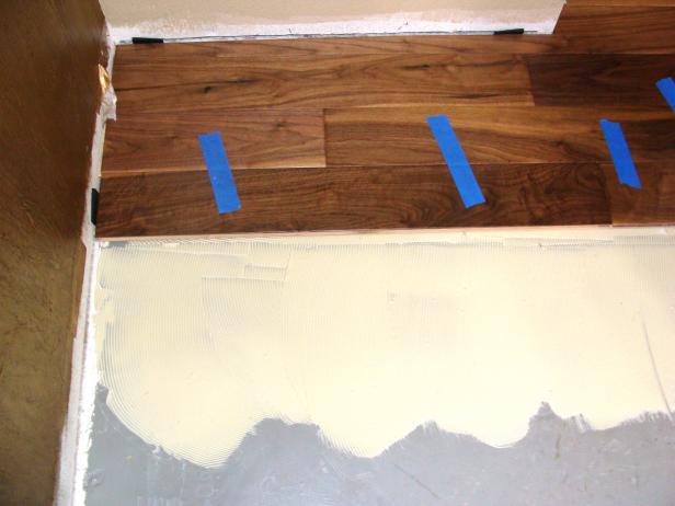 Лепилото за под се използва за реконструкция на пода от твърда дървесина, докато бояджийската лента държи дъските заедно.