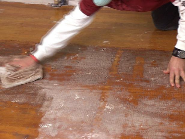 Човек използва парцал, за да помогне на проект за монтаж на пода, използвайки твърда дървесина.