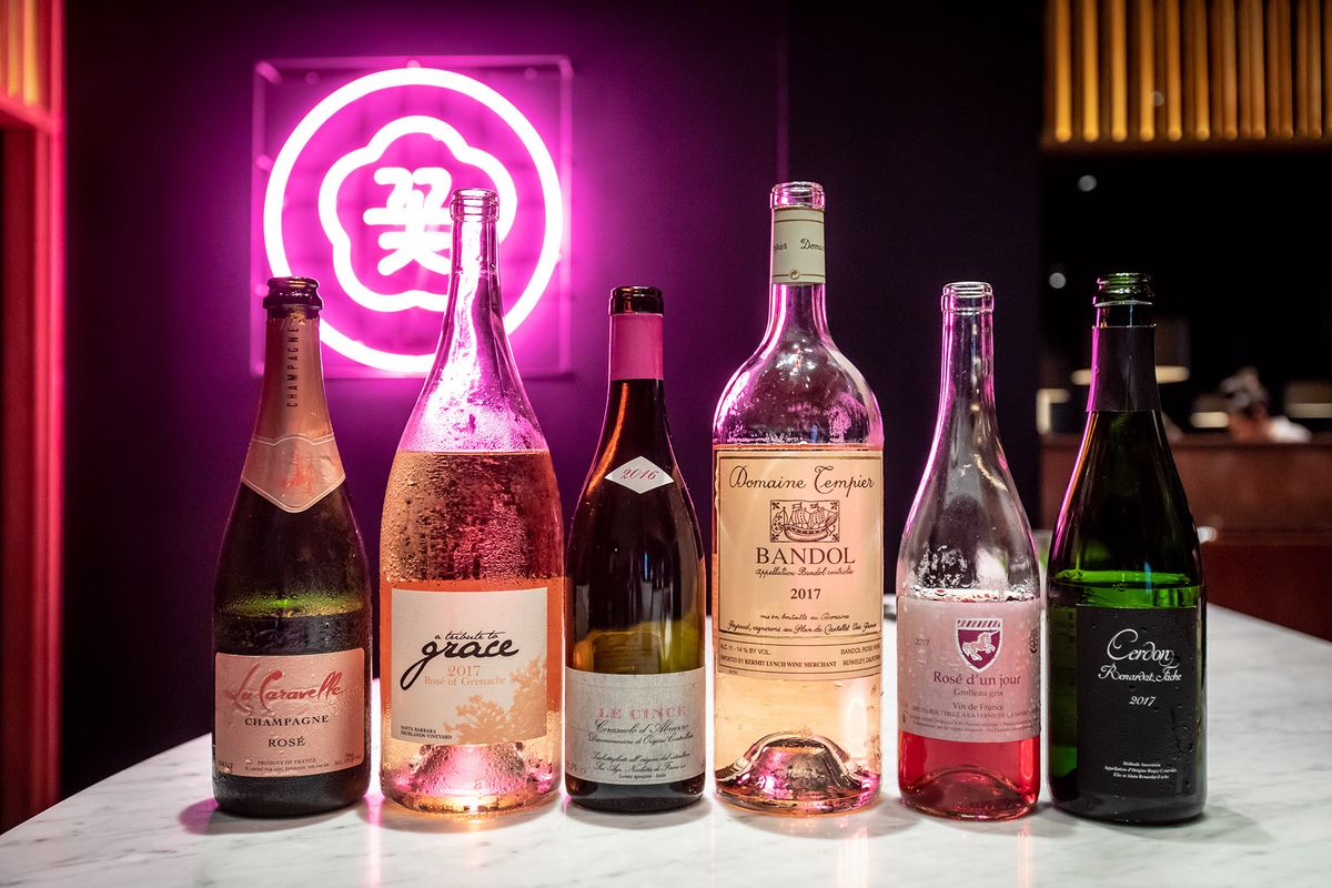 Sešas atvērtas atdzesēta rozā vīna pudeles ar aiz muguras karsti rozā neona zīmi