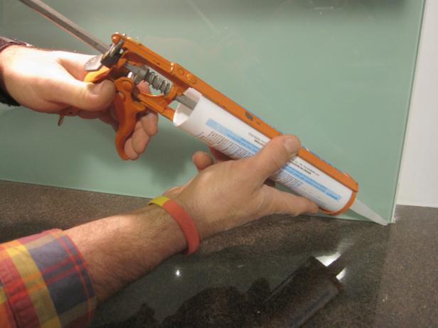 Een siliconenpistool gebruiken om siliconen op de bodem van de glazen achterwand te plaatsen