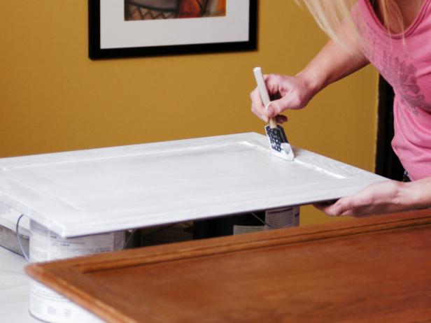 महिला सफेद पेंट का उपयोग करके स्पंज ब्रश से कैबिनेट पेंट करती है।