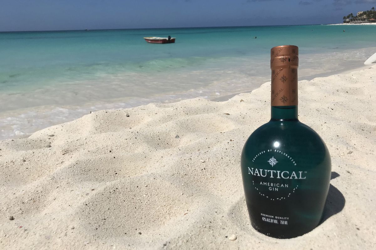Una bottiglia verde scuro in spiaggia di sabbia bianca con acqua turchese