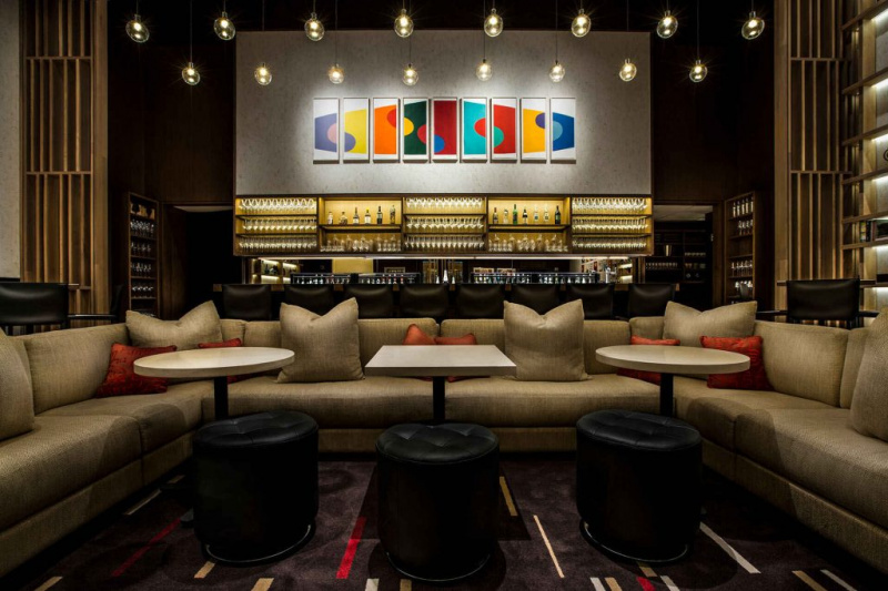   Большой диван с подушками и отдельные столики с круглыми оттоманками перед полностью укомплектованным баром винного бара Aldo Sohm, Нью-Йорк.