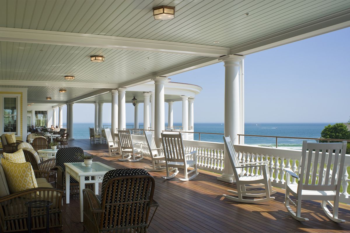 Grande pátio com balconey branco, cadeiras de balanço, móveis de vime e vista para o oceano azul