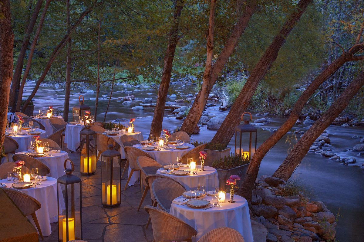 Weiße Tische mit Kerzenlicht zum Abendessen, große Laternen neben einem Bach mit abgerundeten Felsen