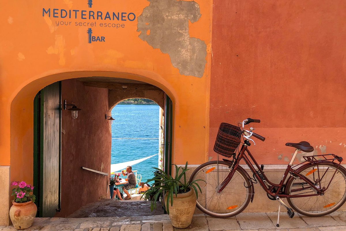 Bicicleta contra una pared naranja, el mar visible a través de la puerta