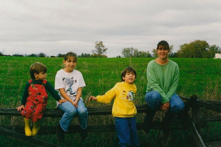 3人の子供とフィールドの前の木製の柵に座っている女性