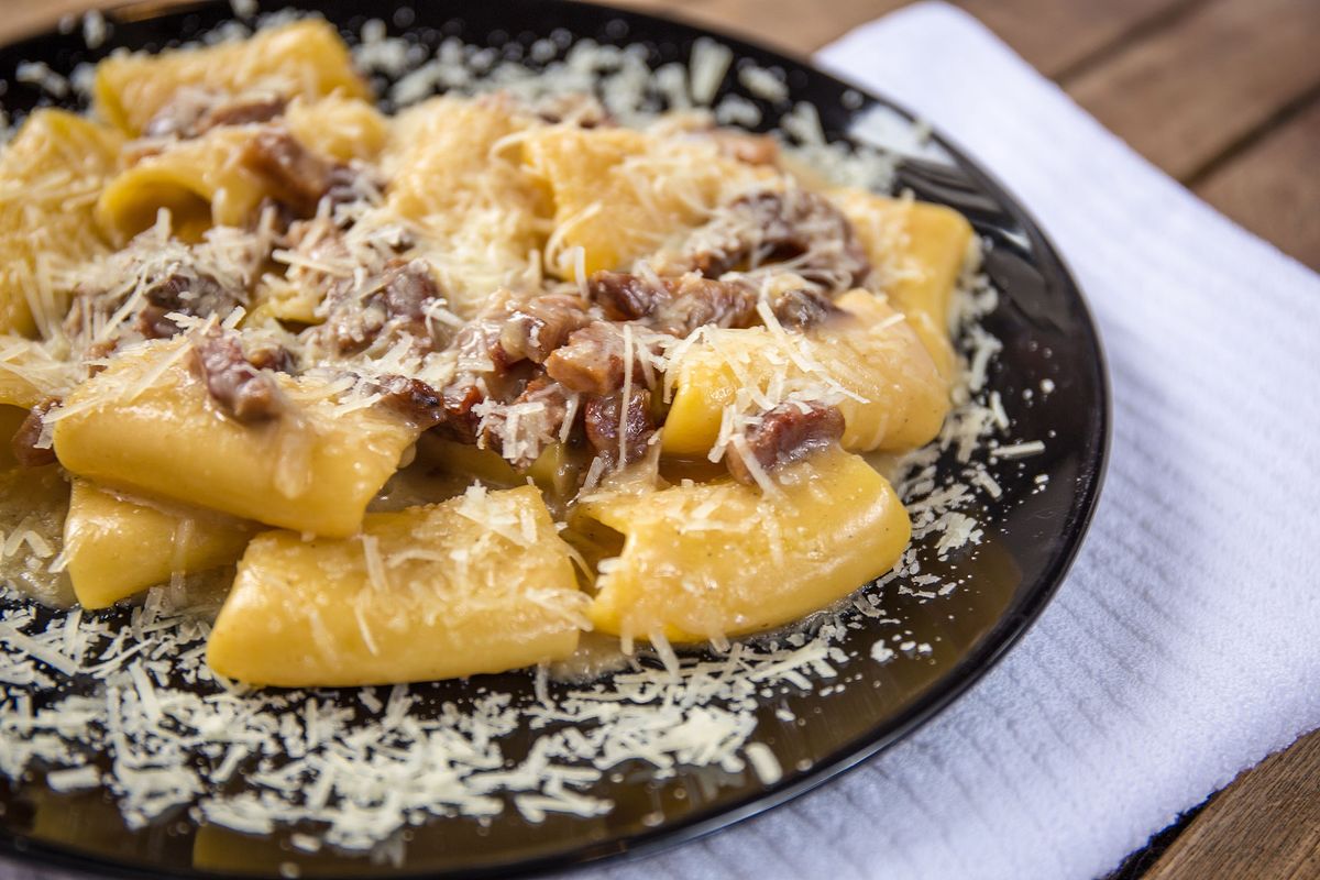 Stor rund pasta toppet med ragu og ost på en sort plade