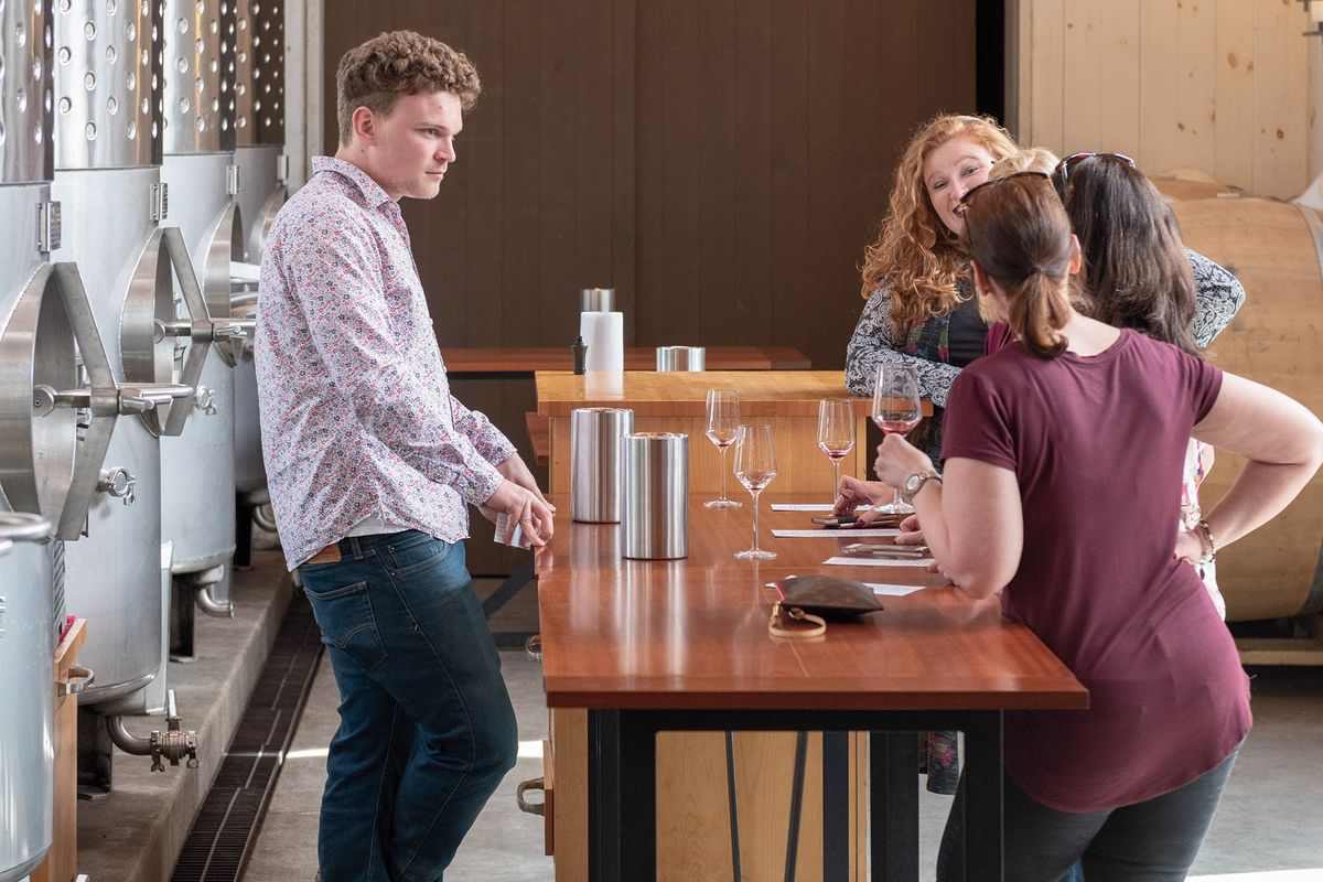 Muškarac i četiri žene kušaju crveno vino za dugačkim drvenim stolom