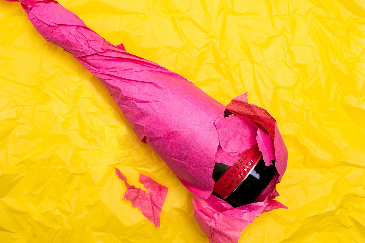 Láhev šampaňského zabalená do růžového hedvábného papíru na zářivě žlutém pozadí