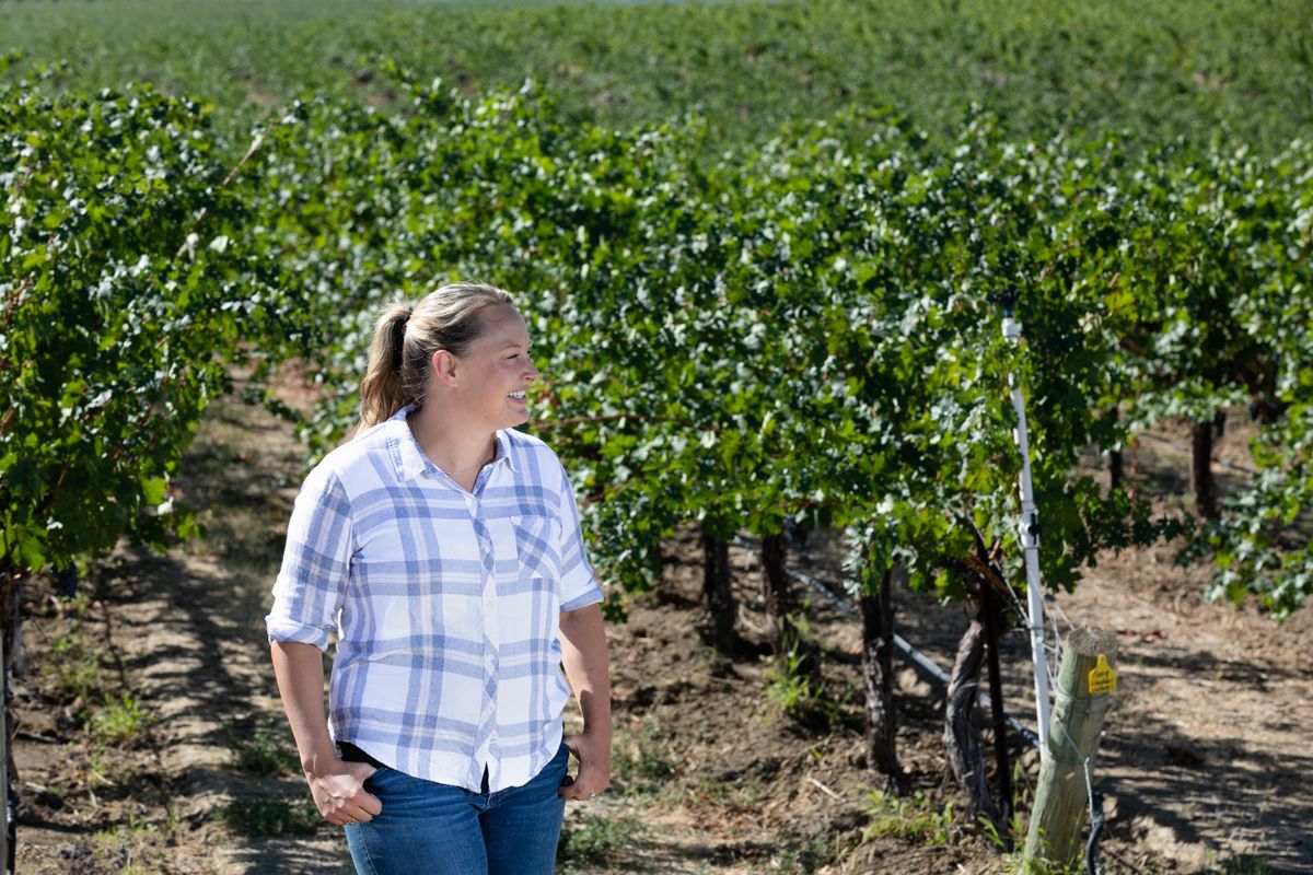 Sievietes rūtainā kreklā stāvot vīna dārza priekšā