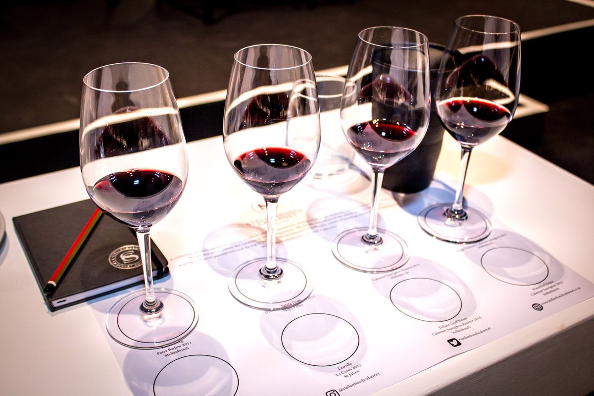 Neljän viinilasin rivi viinin maistelussa, joista jokaisessa on syvän punaviiniä