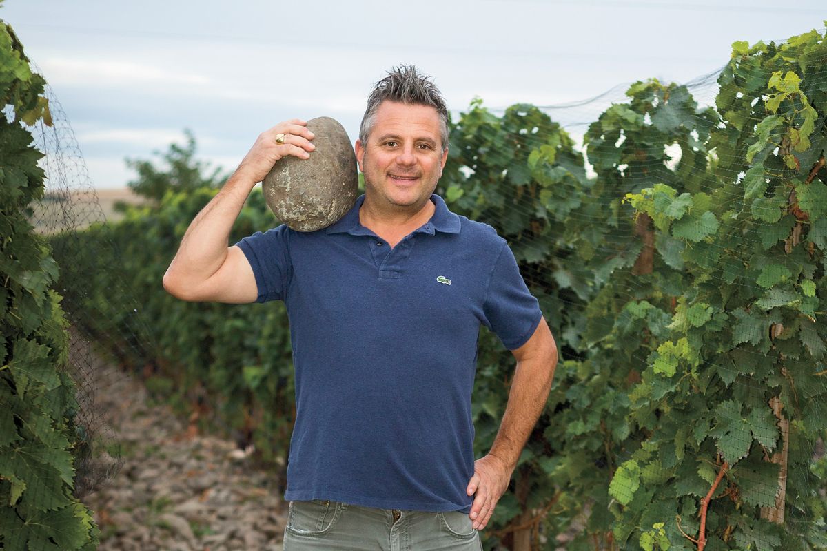Christophe Baron sosteniendo una piedra con forma de huevo en su hombro en un viñedo