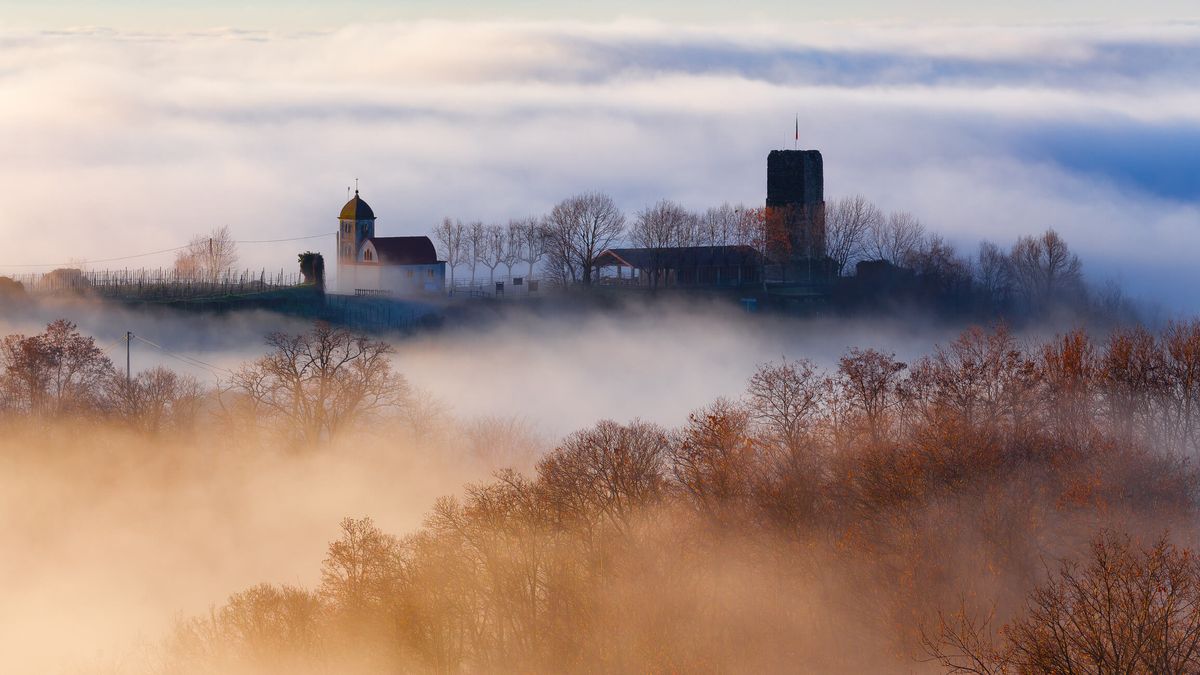 Una iglesia y un edificio sobre niebla y árboles.