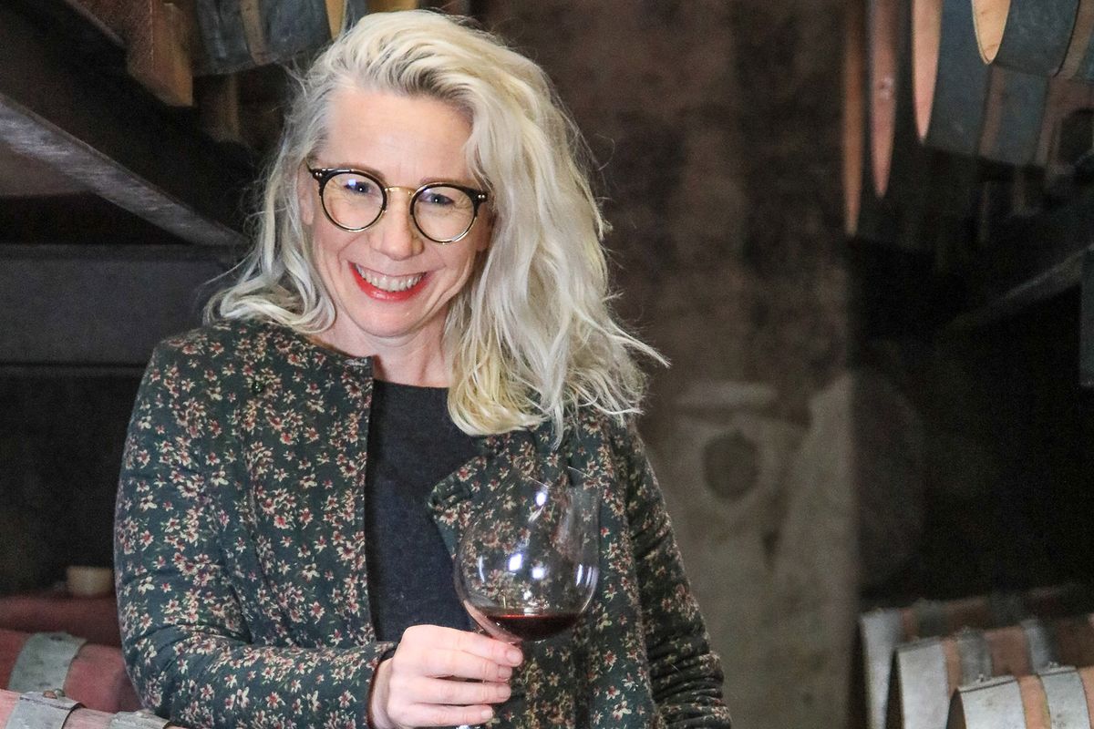 Mujer con gafas sonriendo a la cámara, holidng una copa de vino
