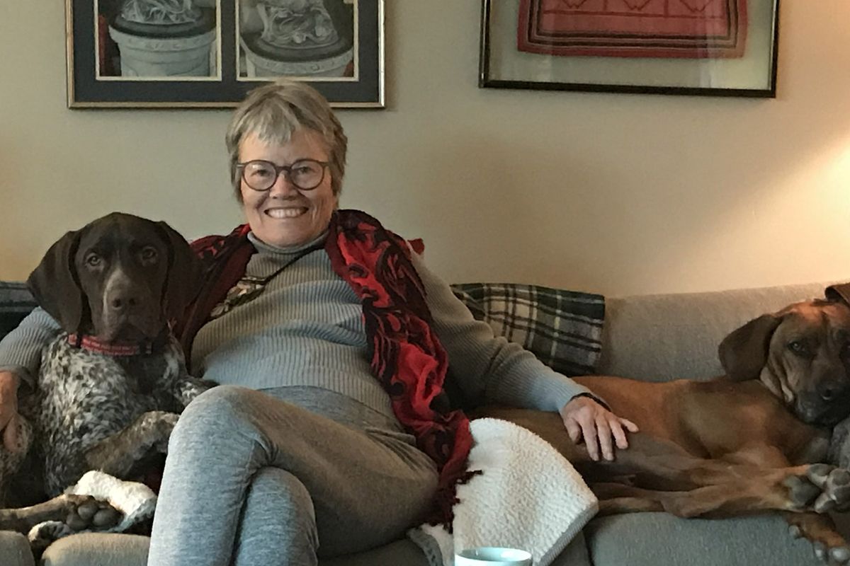 Vyresnė moteris sėdi ant modernios sofos su dviem šunimis